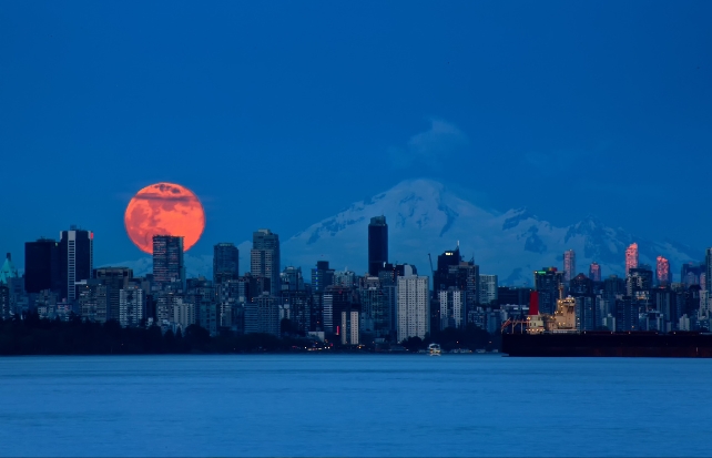 Uma lua vermelha brilhante nascendo atrás do horizonte de uma cidade 