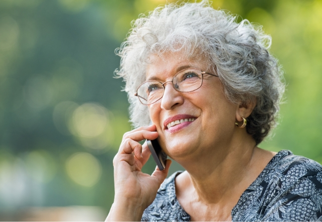 Uma mulher mais velha, com cabelos grisalhos e óculos, falando ao telefone