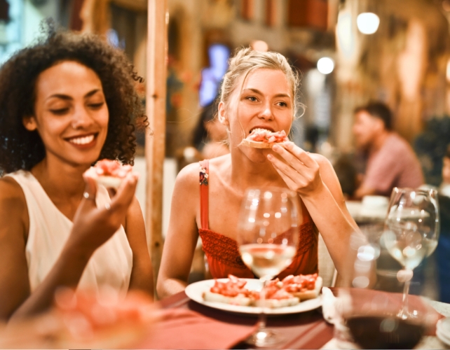 Duas jovens comendo pizza e bebendo vinho