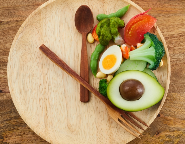 Comida em uma placa de madeira em uma seção com talheres colocados como se fossem ponteiros de um relógio