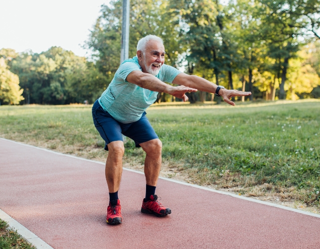 Um homem mais velho agachado com os braços estendidos em um parque