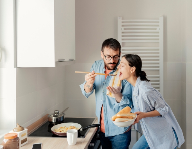 Um jovem casal cozinhando o jantar e saboreando comida em uma colher 