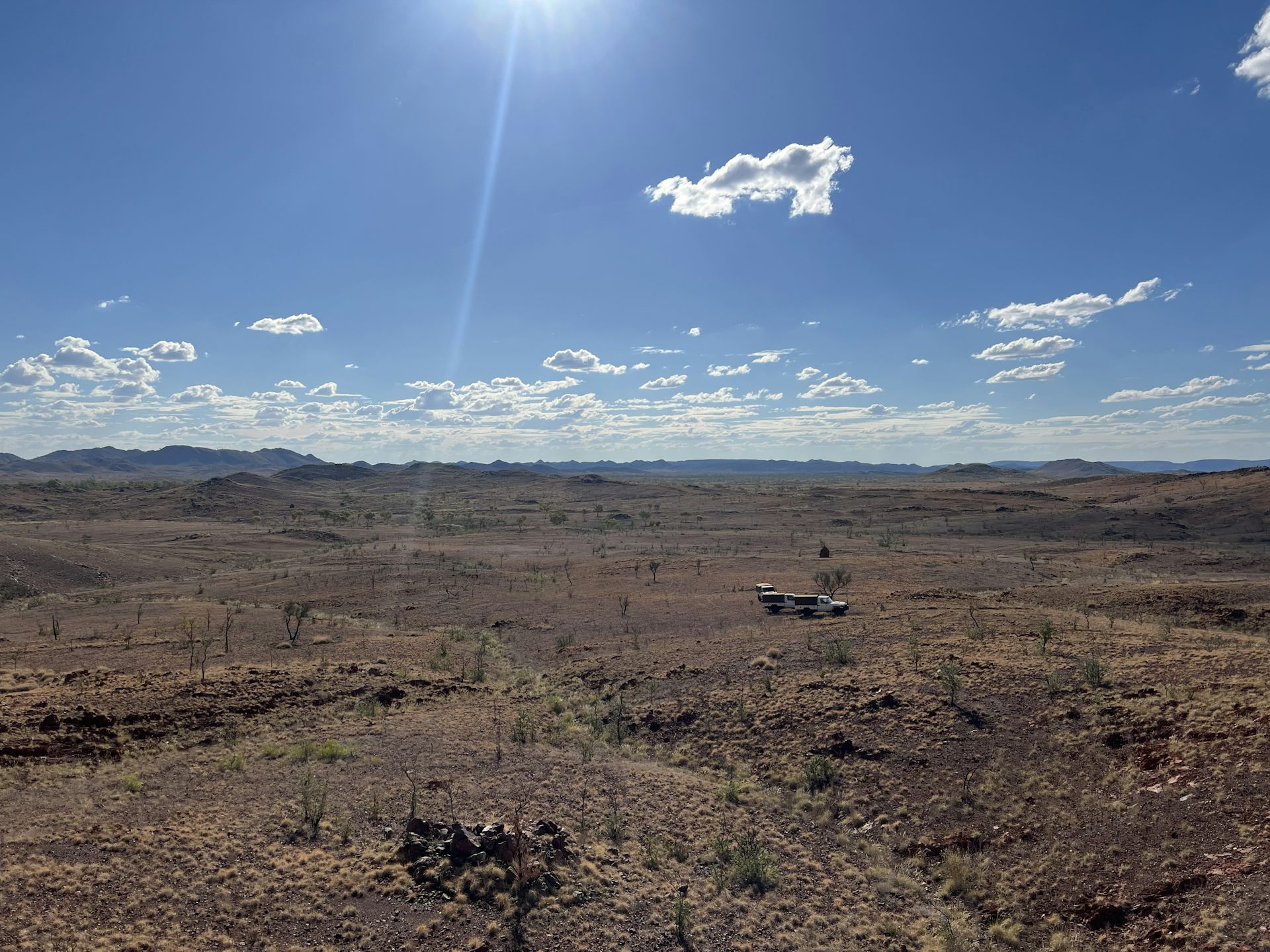 Paisagem aberta, escassamente vegetada, seca e aberta com pequenas colinas distantes sob o céu azul cravejado de nuvens